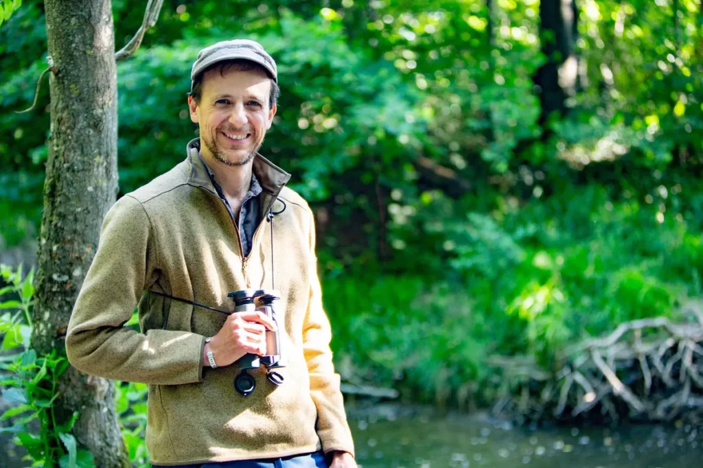 Julien Perrot, fondateur de la revue Salamandre, debout dans la nature avec des jumelles dans la main.
